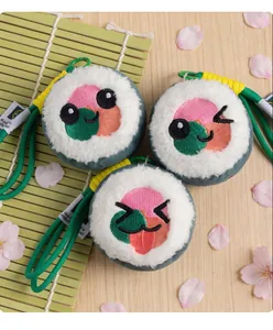 Close-up of three cute sushi roll plush charms with embroidered faces on a bamboo mat