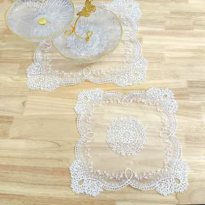Detailed macro shot of white square lace mat with intricate floral vine embroidery