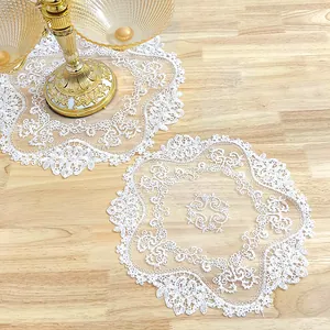 Close-up detail of white circular lace doily with intricate floral embroidery on wood surface