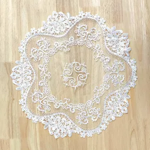 Detail view of white circular lace placemat with intricate hollow floral embroidery.