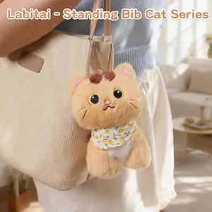 Cute ginger standing kitten plush charm with floral bib hanging on a beige tote bag