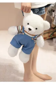 Detail of a soft white plush teddy bear wearing blue denim overalls and a striped shirt.