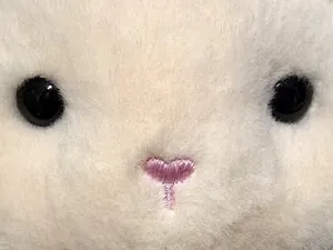 Detalle macro de una oveja de peluche blanca con nariz rosa bordada en forma de corazón