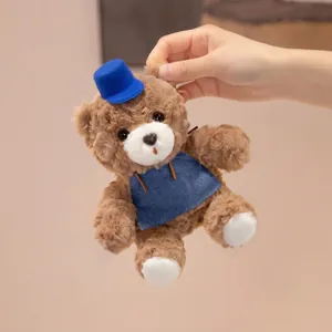 Cute handheld small brown teddy bear plush toy wearing a blue hat and denim apron