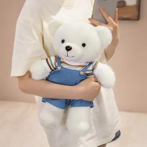 Adorable white teddy bear plush toy wearing a striped shirt and blue denim overalls