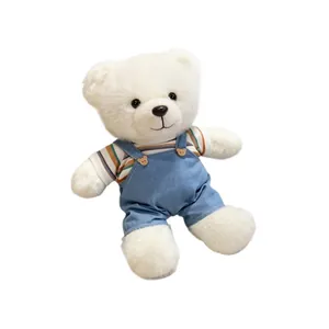 Soft white plush teddy bear wearing striped shirt and denim overalls on white background