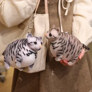 Two chubby grey striped cat plush dolls, one as a keychain on a bag, one held in hands.