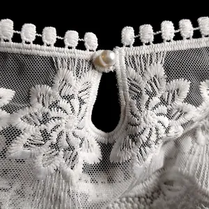 Détail de broderie en dentelle de soie de lait blanche avec un bouton perle élégant.