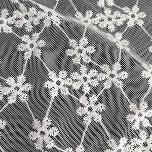 Close-up van wit sneeuwvlok borduurwerk op delicate mesh kant stof textuur.