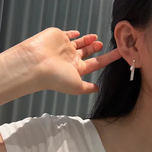 Gros plan de boucles d'oreilles pompon en argent S925 et perle naturelle portées par un mannequin.