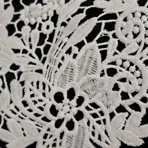 Macro detail of intricate white milk silk embroidered lace floral pattern on black