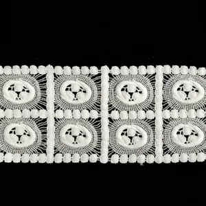Macro detail of white milk silk embroidered lace trim with hollow square floral patterns.