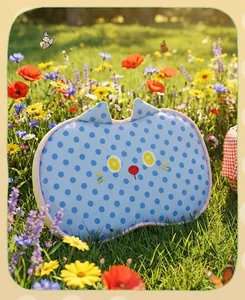 Close-up of a blue polka dot cat-shaped memory foam pillow in a sunny flower meadow.