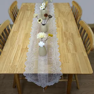 Detailed view of French white embroidered lace table runner on a wooden table