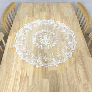 Elegant white circular lace doily with floral embroidery on a light wooden table surface.