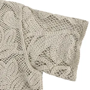 Detailed macro shot of intricate floral lace crochet pattern on a beige top