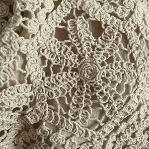 Detailed texture of off-white cotton crochet lace fabric with intricate hollow embroidery