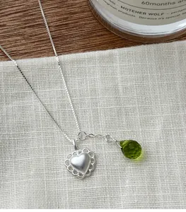 Detailed macro view of matte s925 silver heart and green faceted teardrop necklace charm