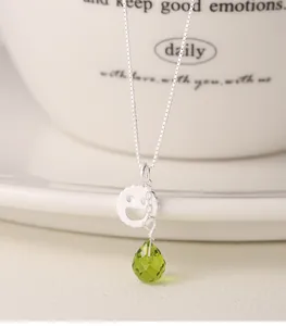 Primo piano di una collana in argento sterling S925 con faccina e cristallo a goccia verde.