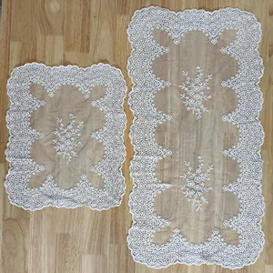 Detail view of two white floral cotton lace embroidered tablecloths on wooden surface