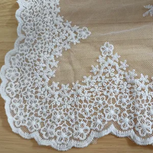 Detailed close-up of white floral cotton lace embroidery on delicate mesh fabric.