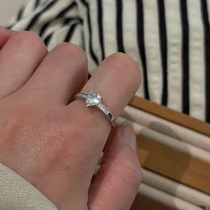 Detailed macro shot of a delicate silver heart-shaped solitaire ring worn on a finger