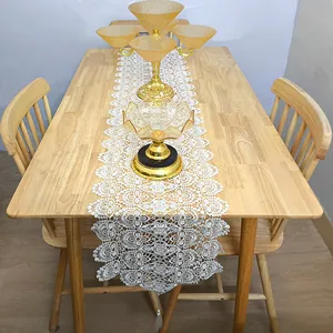 Elegant white lace table runner with embroidery and tassels on a wooden dining table