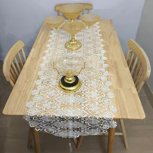 Elegant white lace table runner with hollow embroidery and tassel detail on wooden table