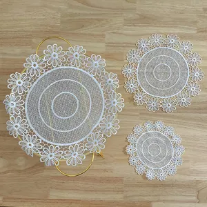 Macro shot of three round white lace coasters with floral embroidery on a wood table