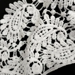 Macro detail of white milk silk embroidery lace with intricate floral paisley patterns.