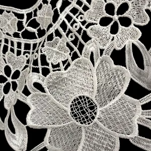Macro view of white polyester embroidered hollow lace with intricate floral pattern details.