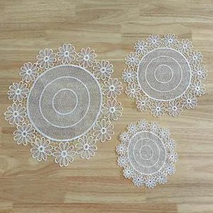 Set of three white embroidered lace floral round placemats on a light wooden table background