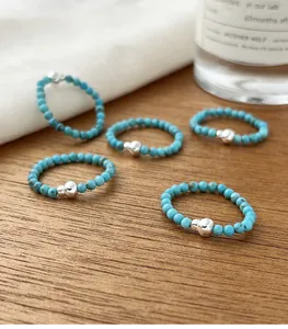 Detailed view of five turquoise beaded rings with silver gourd charms on wood surface.