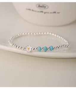 Gros plan d'un bracelet en perles d'argent avec breloque marguerite et turquoise