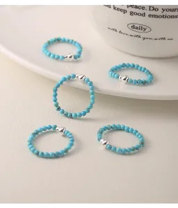 Detail view of handmade turquoise bead rings with silver gourd charm on a white surface