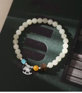 Detail eines handgefertigten Hetian-Jade-Armbands mit silbernem Schaukelpferd und Bernstein.