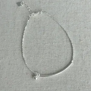 Detail of a textured S925 silver bracelet with a small ball charm and curved bar