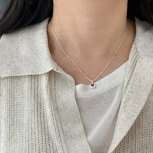 Close-up detail of a minimalist s925 silver necklace with a red heart-shaped pendant