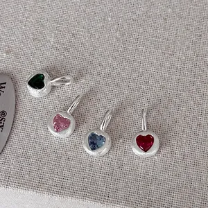 Macro view of four colorful heart gemstone pendants in textured S925 silver on linen.