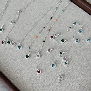 S925 sterling silver heart pendants with colorful rhinestones on a linen background