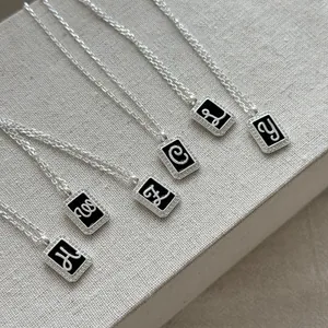 Detailed view of S925 silver square pendants with cursive letters on enamel
