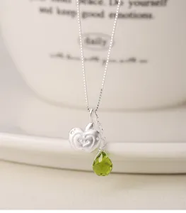 Close-up of S925 silver necklace with apple pendant and green teardrop crystal