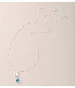Dettaglio di una collana in argento con ciondolo sorridente e perla a goccia blu.