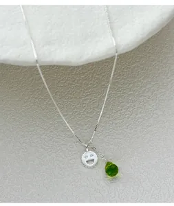 Primo piano di un ciondolo in argento S925 con faccina sorridente e goccia verde sfaccettata