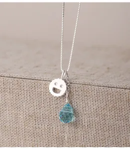Dettaglio macro di collana in argento S925 con pendente smiley e pietra blu a goccia