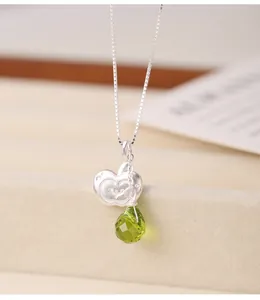 Close-up of s925 silver necklace with apple pendant and green teardrop crystal detail.