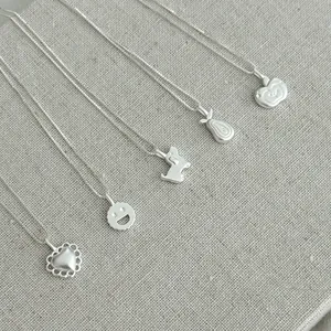 Detailed view of five s925 silver necklaces with various cute pendants on linen texture
