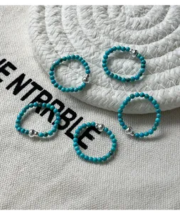 Macro detail view of turquoise beaded elastic rings with silver accent beads and woven backdrop.