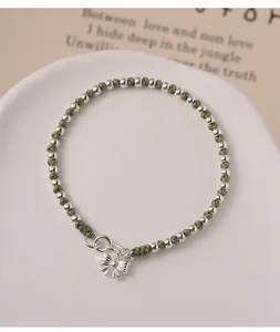 Close-up detail of a green braided cord bracelet featuring silver beads and a bow pendant