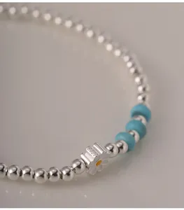 Détail d'un bracelet en argent S925 avec pendentif marguerite et perles turquoises.